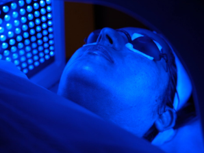 A patient receiving a laser facial treatment under blue light effects while using spectacles.