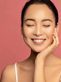 Happy woman is using cream on her face, showing a skincare routine for even toned skin on her face