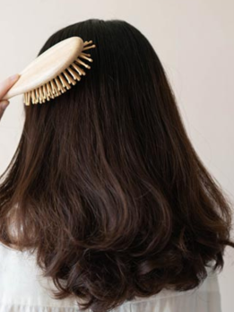 Lady brushing her long, voluminous hair with a comb shows she has got hair regrowth treatment.