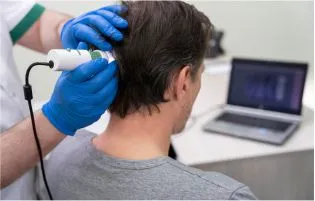 A man in a clinical setting undergoing treatment for hair loss from a hair care specialist.
