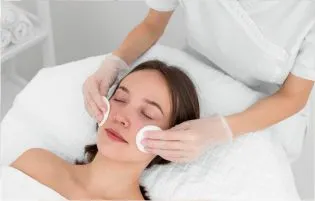 A dermatologist massages a woman's skin following a procedure to remove pimples from her face.