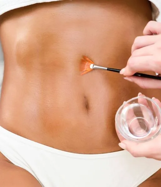 A skin care specialist attends to the patient's skin texture by gently applying oil to her stomach