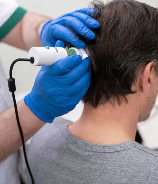 A man in a clinical setting undergoing treatment for hair loss from a hair care specialist.