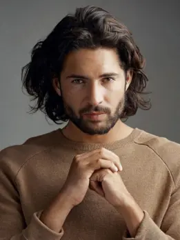 Posing for a picture, the man with the long hair and beard exudes a more refined appearance.