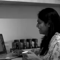 A woman sitting at a table, working on her laptop while attending a Microsoft Teams meeting.