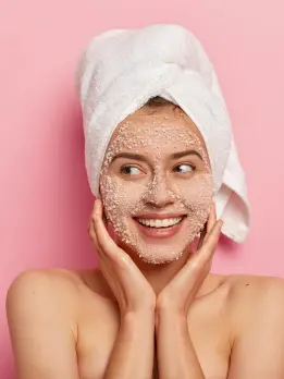 A woman receives skin exfoliation therapy while wearing a face mask and a cloth over her scalp.