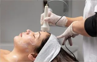 A skin care specialist is treating a patient with laser machine while wearing white coat & gloves.