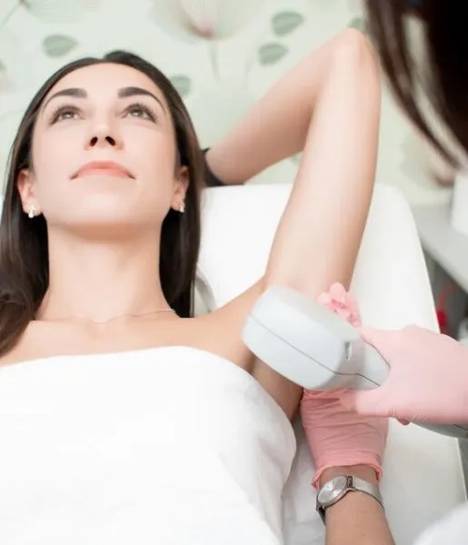 A patient lies down and relaxes while a doctor removes hair from her underarms in a clinic.