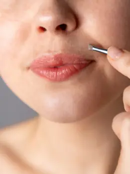 A woman applies cream with a brush after receiving upper lip hair reduction treatment, looking nice.